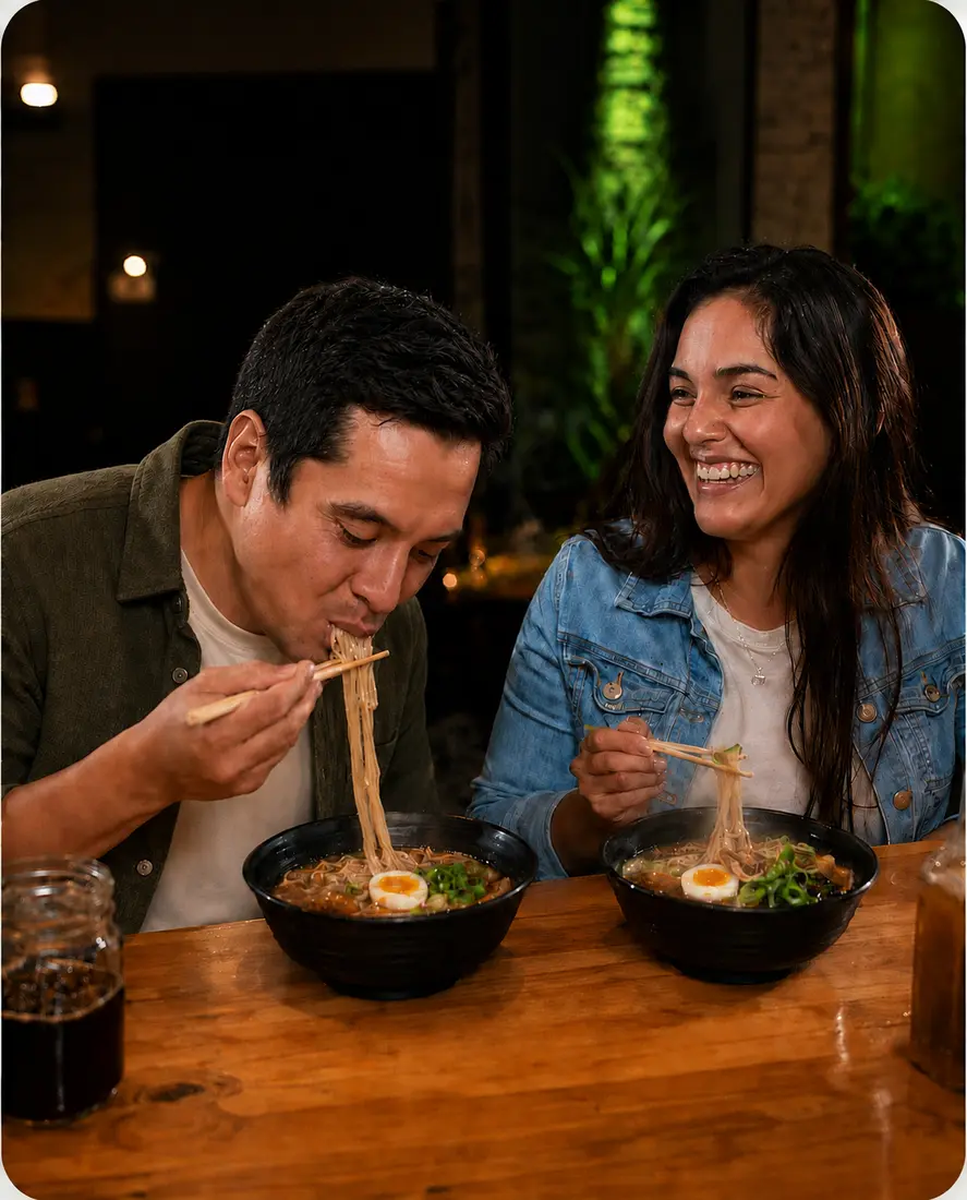 Two friends at the Joren counter, one laughing while the other is focused on eating ramen